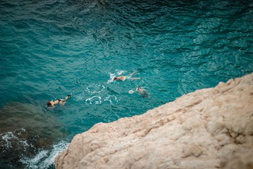 A high angle shot of different people swimming in the ocean next to a cliff