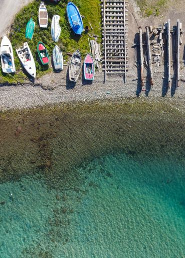 An aerial shot of a crystal clear water and rocky beach with colorful fishing boats in summer