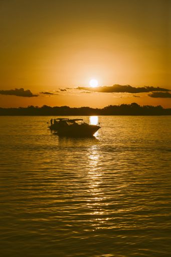 A mesmerizing view of a sailboat moored on a tranquil body of water, illuminated by the warm glow of the setting sun