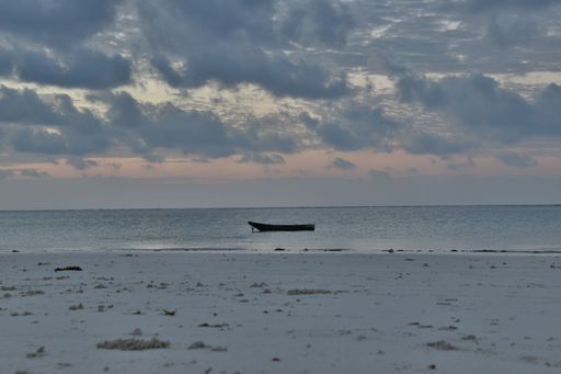 A white fishing boat is adrift in a serene, crystal-clear ocean, illuminated by the sun's warm rays