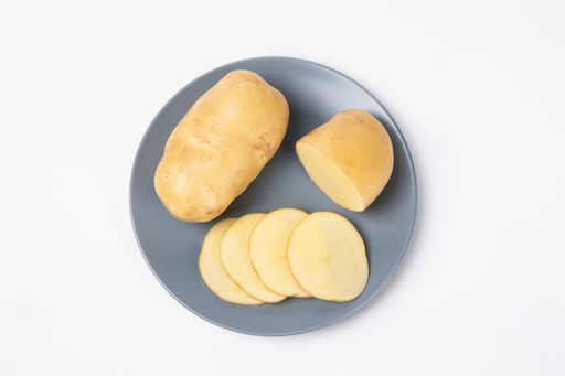 A top view of raw potatoes and cut pieces on the plate isolated on white background