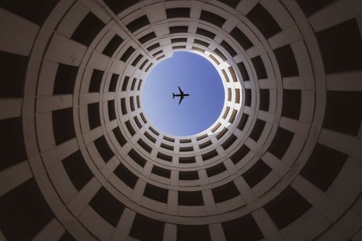 A low angle of an airplane soaring high above a contemporary spiral shaped building