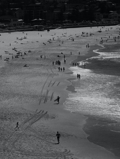 A vertical grayscale shot of a beach populated by people walking around