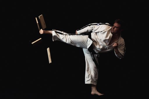 A young man is performing a martial arts maneuver on a solid black background, showcasing his expertise in the art form