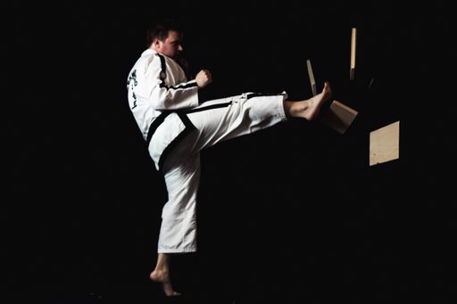 A young man is performing a martial arts maneuver on a solid black background, showcasing his expertise in the art form