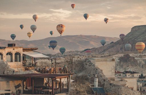 A beautiful view of colorful hot air balloons floating in the sky above the buildings and mountains.