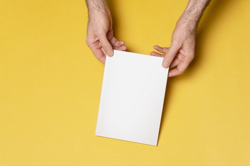 A top view of male hands holding a closed book-catalog with blank cover on yellow background, mockup series template ready for your design