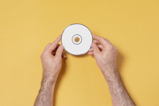 A top view of male hands holding a blank CD-DVD in front of yellow background, editable mockup template for your design