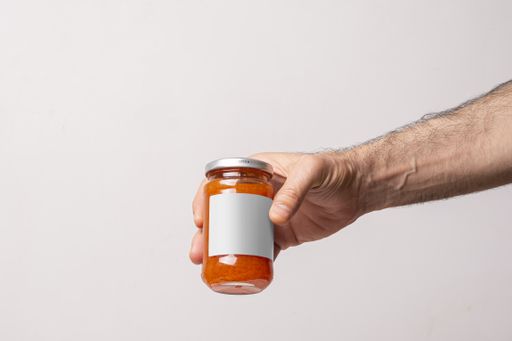 A male hand holding a juicy homemade carrot jar on a white background, editable mock-up series template ready for your design