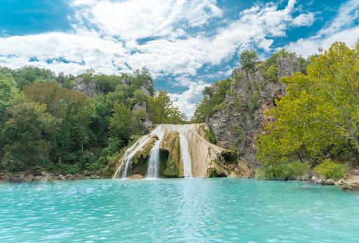 A beautiful shot of a lake with thin waterfalls surrounded by greenery and mountains in the background