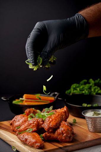 An overhead shot of a wooden board featuring a plate of chicken wings topped with freshly cut green onions