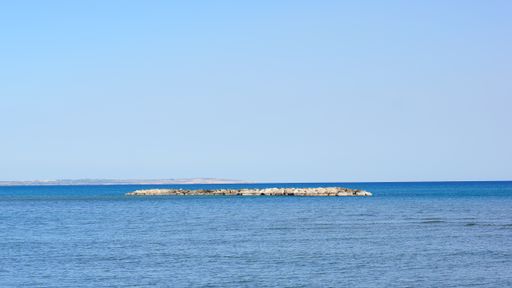 A beautiful shot of a small land in the middle of an ocean under the blue sky