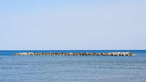 A beautiful shot of a small island covered in stones in the middle of a lake under the blue sky