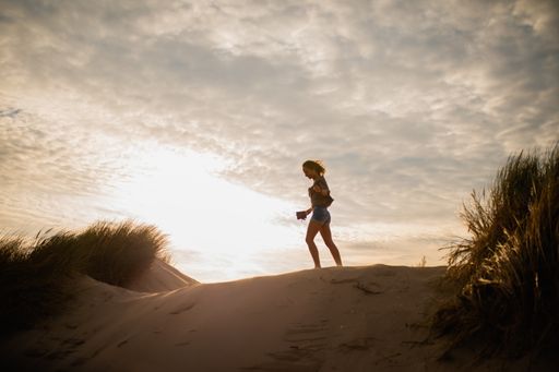 A low angle shot of the silhouette of a woman walking on sand during sunset