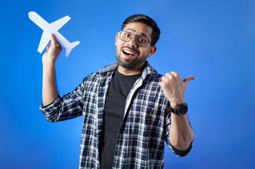 Airplane, vacation, journey. Indian adult student holding paper airplane and pointing with thumb finger.