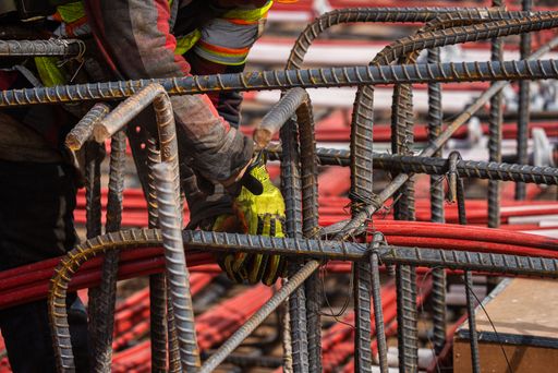 A construction worker is seen in the foreground, hard at work with a set of large steel bars in the background
