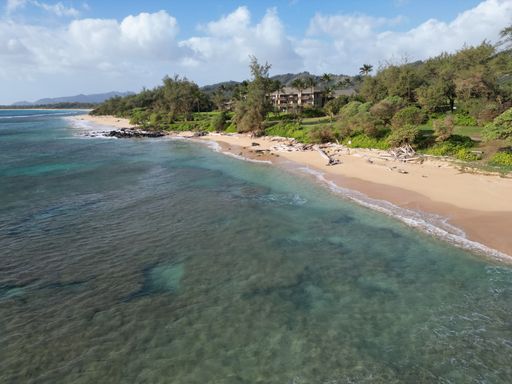 An aerial view of a beach surrounded by the sea and greenery under a blue cloudy sky