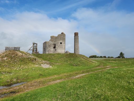 A beautiful scenic view of an old abandoned castle atop a lush green hill with a vibrant rainbow stretching across the sky