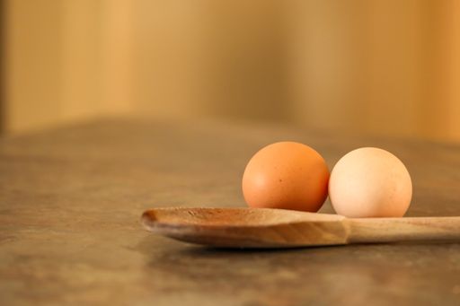 A closeup shot of two eggs and a wooden spoon on a kitchen table with blurred background