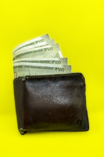A top view of a leather wallet with five hundred rupee notes on vibrant yellow surface