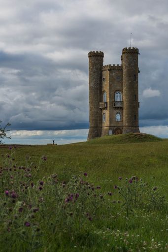 A tall stone tower is silhouetted against a cloudy sky on the green meadow