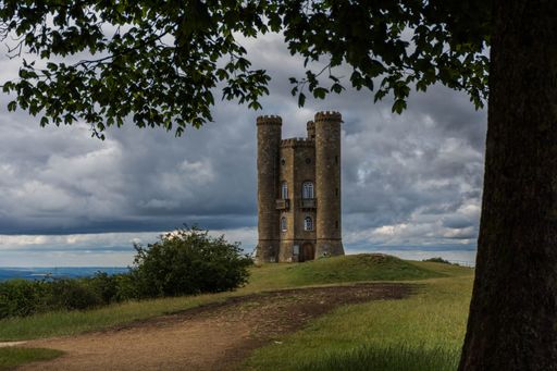 A tall stone tower is silhouetted against a cloudy sky on the green meadow