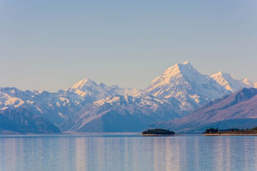 An idyllic landscape featuring a large mountain range reflected in the waters of a tranquil lake with a small island in the foreground