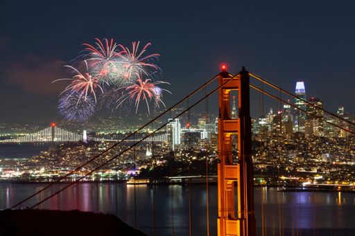 A breathtaking nighttime landscape in a city setting featuring brilliant fireworks illuminating the night sky above a bridge