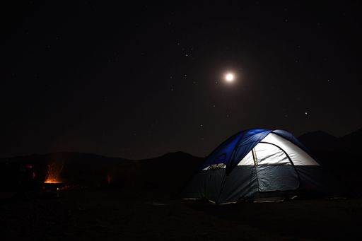A camping tent illuminated by a full moon in a starry sky