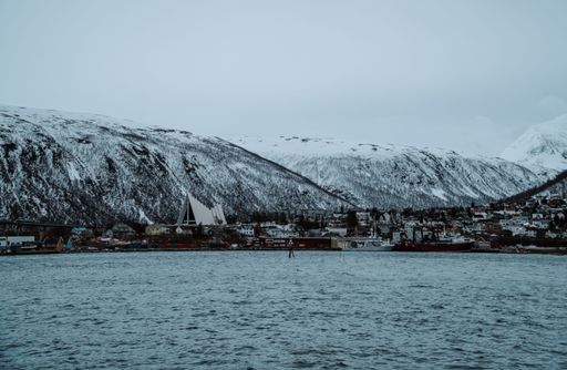 A stunning winter scene of a peaceful shoreline in Tromso, Norway, featuring picturesque snow-covered mountains in the background