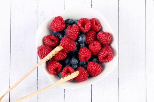 A top view of raspberries and blueberries in a bowl with a wooden kitchen tool