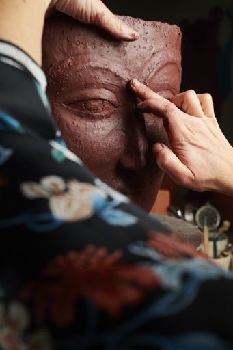 A closeup shot of hands sculpting a clay vase with a face