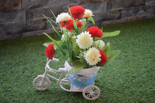 A miniature bicycle planter with white and red flowers in a basket on the grass
