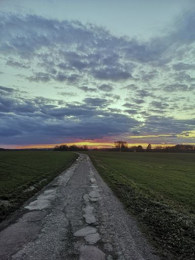 A lonely rural street through the fields under a cloudy sky during sunset