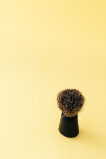 A vertical shot of a shaving brush isolated on a yellow surface