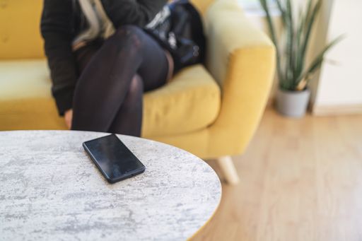 A black phone on a table with a young woman sitting in a background