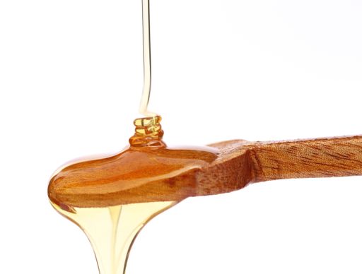 A closeup of a wooden spoon with a pouring stream of honey isolated on a white background.
