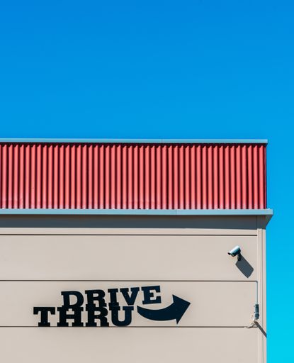A vertical shot of a building wall with Drive-Thru written on it against a clear blue sky background