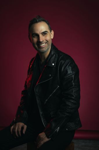 A studio portrait of a Caucasian man wearing a black leather jacket on a red background
