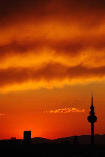 A vertical silhouette of a tower gleaming against the orange cloudy sky during sunset