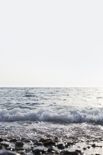 A vertical shot of the sea with beautiful waves and clear white sky - view from the beach