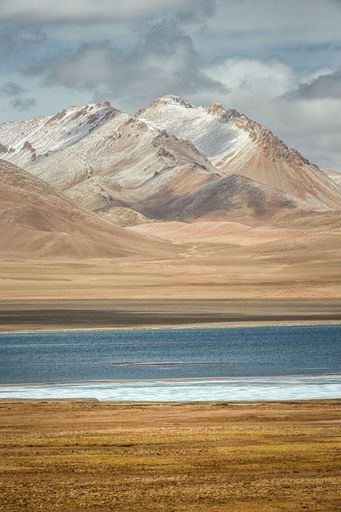 A scenic winter landscape featuring a tranquil lake in the foreground and snow-capped mountains in the background