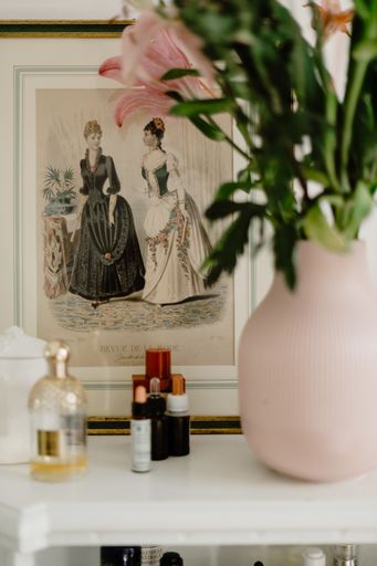 A vertical shot of a framed artwork on a shelf with beauty products and a flower bouquet on it