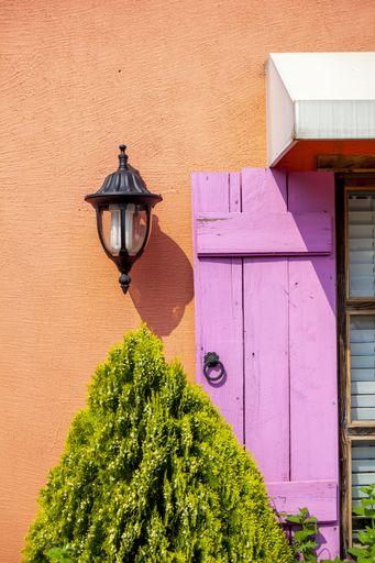 A vertical shot of a lamp on a colorful building with a pink wooden window under the sulight