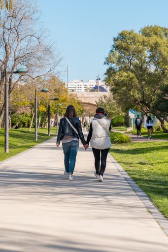 A rearview of two women holding hands while walking in the Turia river park in Valencia, Spain