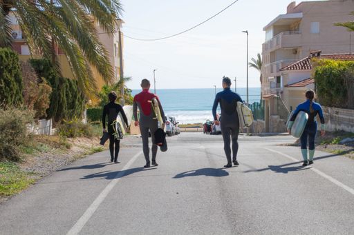 Four Spanish surfers with surfboards walking on a street towards a Mediterranean beach in Alicante.