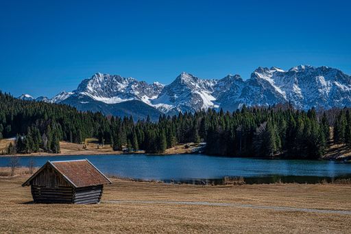 A small picturesque cottage situated on the shore of a tranquil lake, with a breathtaking backdrop of snow-capped mountains