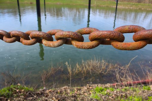 A closeup shot of a rusty metal chain near the calm lake