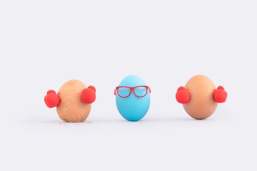 A closeup shot of eggs with boxing gloves and a referee on a white background