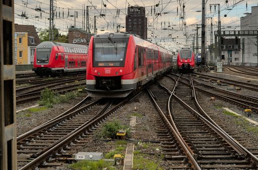 A view of the Cologne Main Train Station in Germany featuring multiple passenger trains with overhead electric wiring
